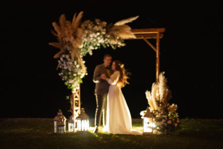 bride and groom against the backdrop of an evening wedding arch with warm live fireの写真素材