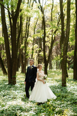 the groom and the bride are walking in the forest on a bright dayの写真素材