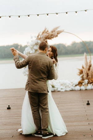 the first wedding dance of the bride and groom on the pier near the river, against the backdrop of the wedding archの写真素材