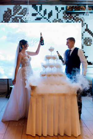 newlyweds at a banquet pour champagne into a pile of glasses for guestsの写真素材