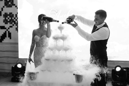 newlyweds at a banquet pour champagne into a pile of glasses for guestsの写真素材