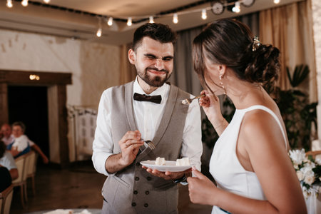 newlyweds happily cut, laugh and taste the wedding cakeの写真素材