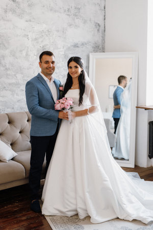 groom in a blue suit with a bow tie and the bride in a tight white dress in a bright studioの写真素材