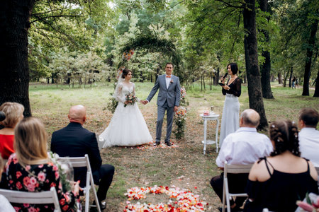 wedding ceremony of the marriage of a guy and a girl against the backdrop of an arch on a forest pathの写真素材