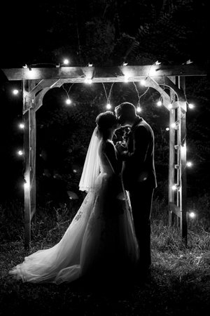 bride and groom against the backdrop of an evening wedding arch with warm lightsの写真素材