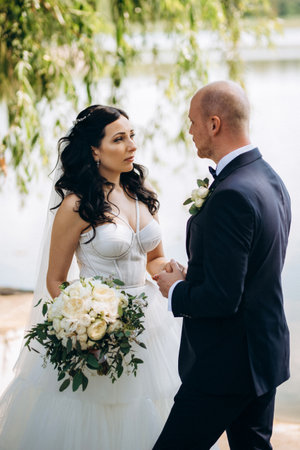 A black-haired bride in a white dress and a groom in a blue suit with a bow tie on a walk in the park on their wedding dayの写真素材
