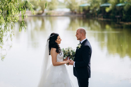 A black-haired bride in a white dress and a groom in a blue suit with a bow tie on a walk in the park on their wedding dayの写真素材