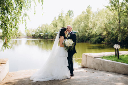 A black-haired bride in a white dress and a groom in a blue suit with a bow tie on a walk in the park on their wedding dayの写真素材