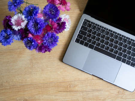 Top view of the workplace with a laptop and flowers cornflowers.の写真素材
