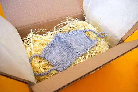 Knitted gray face mask in an open box on a yellow background. Home delivery.の写真素材