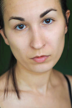 close-up of a young brunette woman looking at the camera on a green backgroundの写真素材