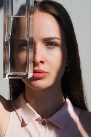 Conceptual surreal portrait of a young Caucasian woman looking through a vase of water. Hard bright light. Optical illusion, object distortionの写真素材