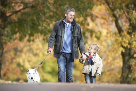 Man With Young Son Walking Dog Through Autumn Parkの写真素材