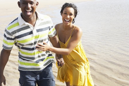Romantic Young Couple Running Along Shoreline Of Beach Holding Handsの写真素材