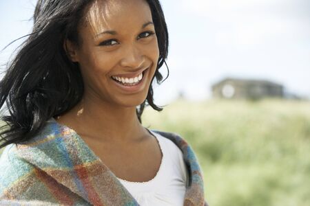 Thoughtful Young Woman Standing On Beach Wrapped In Blanketの写真素材