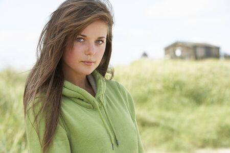 Thoughtful Young Woman Standing On Beach Wearing Hooded Top With Old Beach Hut In Distanceの写真素材