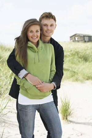 Romantic Young Couple Standing By Dunes With Beach Hut In Distanceの写真素材