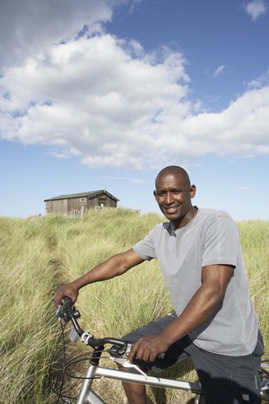 Young Man Riding Mountain Bike By Dunes With Old Beach Hut In Distanceの写真素材