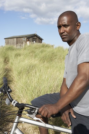 Young Man Riding Mountain Bike By Dunes With Old Beach Hut In Distanceの写真素材