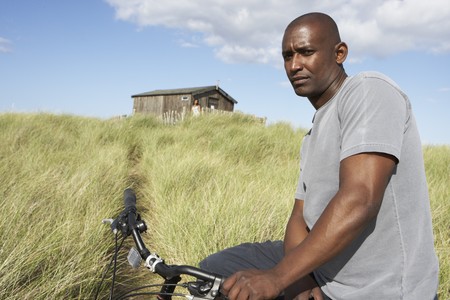 Young Man Riding Mountain Bike By Dunes With Old Beach Hut In Distanceの写真素材
