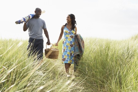 Young Couple Carrying Picnic Basket And Windbreak Walking Through Dunesの写真素材