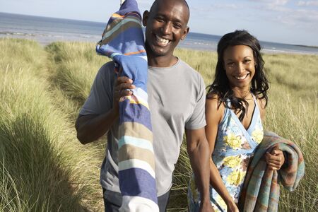 Young Couple Carrying Picnic Basket And Windbreak Walking Through Dunesの写真素材