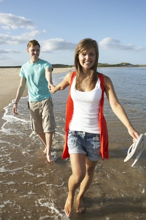 Romantic Young Couple Walking Along Shoreline Of Beach Holding Handsの写真素材