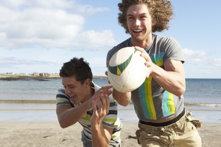 Two Teenage Boys Playing Rugby On Beach Togetherの写真素材