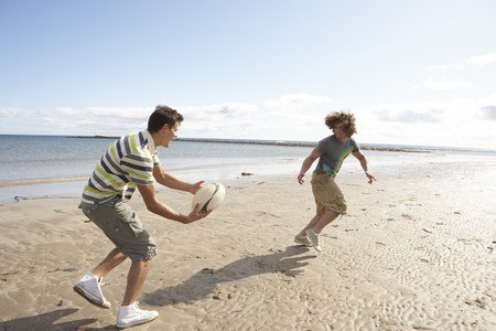 Two Teenage Boys Playing Rugby On Beach Togetherの写真素材