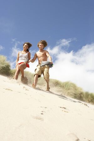 Young Couple Running Down Sand Dune On Beachの写真素材