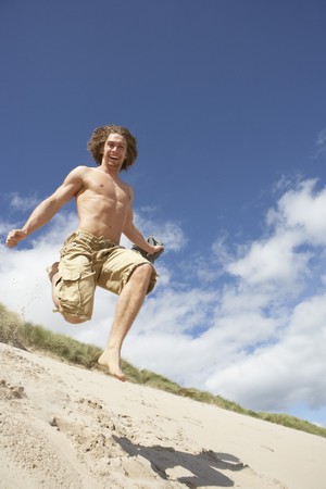 Young Man Running Down Sand Dune On Beachの写真素材