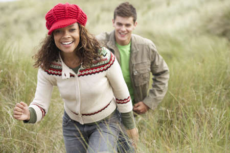 Teenage Couple Walking Through Sand Dunes Wearing Warm Clothingの写真素材