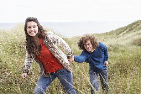 Young Couple Walking Through Sand Dunes Wearing Warm Clothingの写真素材