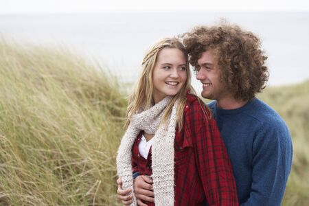Teenage Couple Walking Through Sand Dunes Wearing Warm Clothingの写真素材