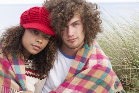 Young Couple Sitting In Sand Dunes Wrapped In Blanketの写真素材