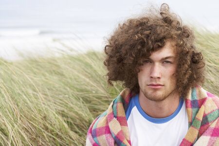 Young Man Standing In Sand Dunes Wrapped In Blanketの写真素材