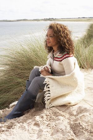 Young Woman Sitting In Sand Dunes Wrapped In Blanketの写真素材
