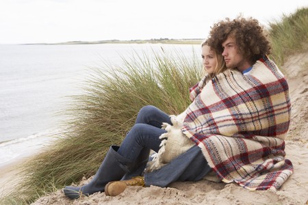 Teenage Couple Sitting In Sand Dunes Wrapped In Blanketの写真素材