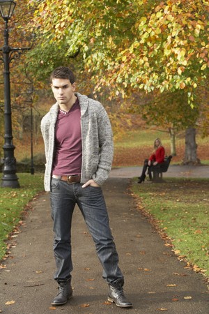Teenage Boy Standing In Autumn Park With Female Figure On Bench In Backgroundの写真素材