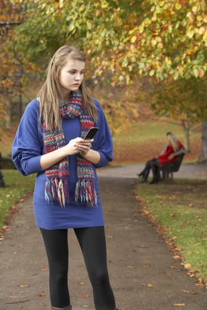 Unhappy Teenage Girl Standing In Autumn Park With Couple On Bench In Backgroundの写真素材