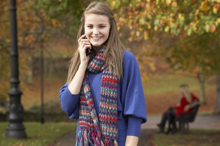 Teenage Girl On Mobile Phone In Autumn Park With Couple On Bench In Backgroundの写真素材