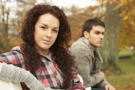 Close Up Of Teenage Couple Sitting On Bench In Autumn Parkの写真素材