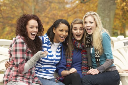 Group Of Four Teenage Girls Sitting On Bench In Autumn Parkの写真素材
