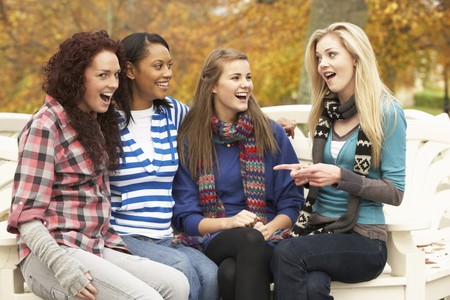 Group Of Four Teenage Girls Sitting On Bench In Autumn Parkの写真素材