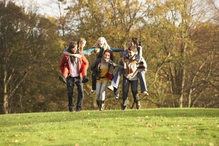 Group Of Teenage Friends Having Piggyback Rides In Autumn Landscapeの写真素材