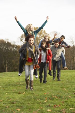 Group Of Teenage Friends Having Piggyback Rides In Autumn Landscapeの写真素材