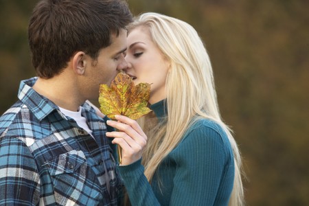 Romantic Teenage Couple Kissing Behind Autumn Leafの写真素材