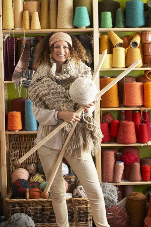 Woman Wearing Knitted Scarf Standing In Front Of Yarn Display Holding Giant Needles And Ball Of Woolの写真素材