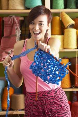 Young Woman Holding Knitting Standing In Front Of Yarn Displayの写真素材