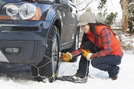 Woman Putting Snow Chains Onto Tyre Of Carの写真素材